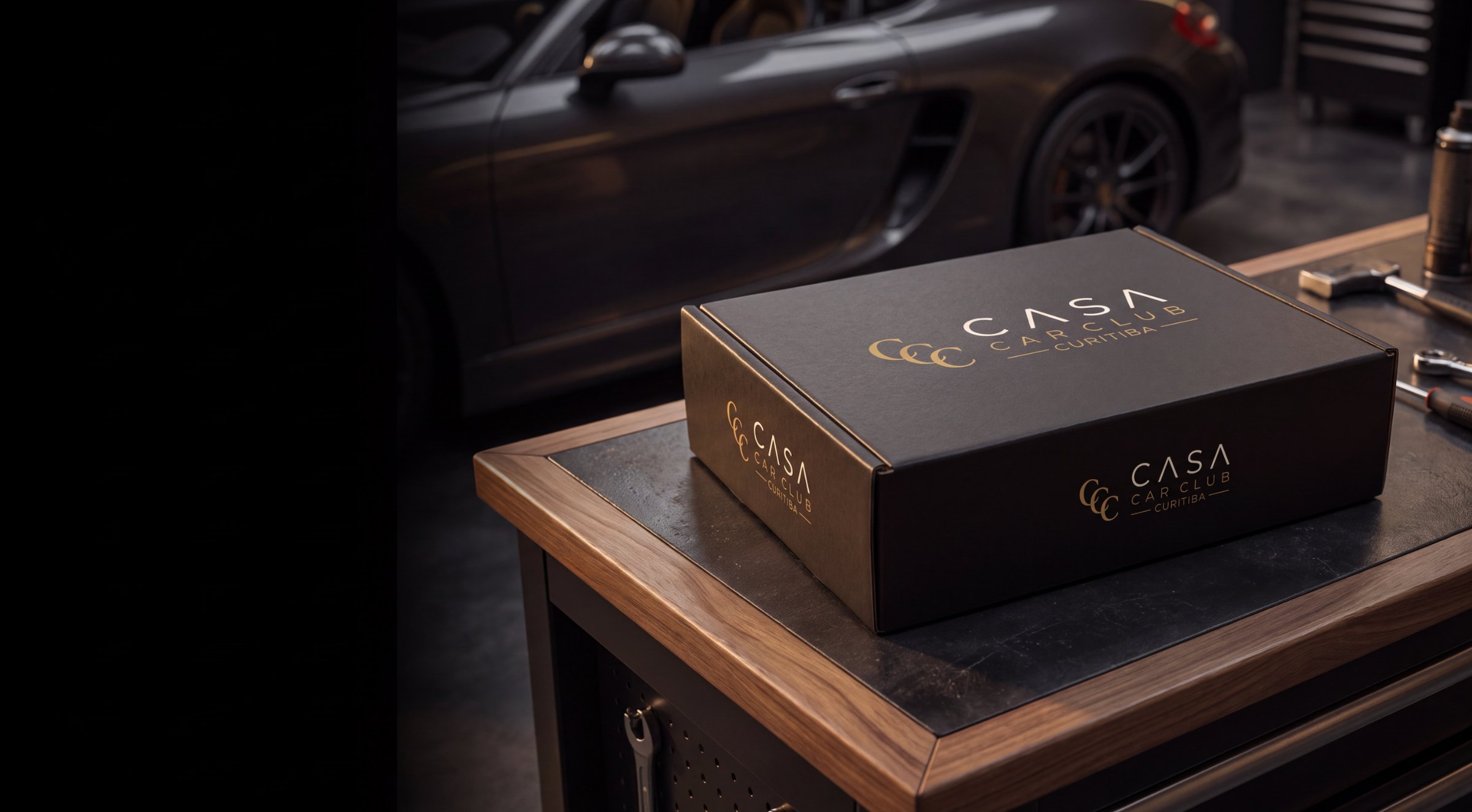 Caixa CASA Box sobre uma bancada de oficina, com um carro esportivo escuro ao fundo.