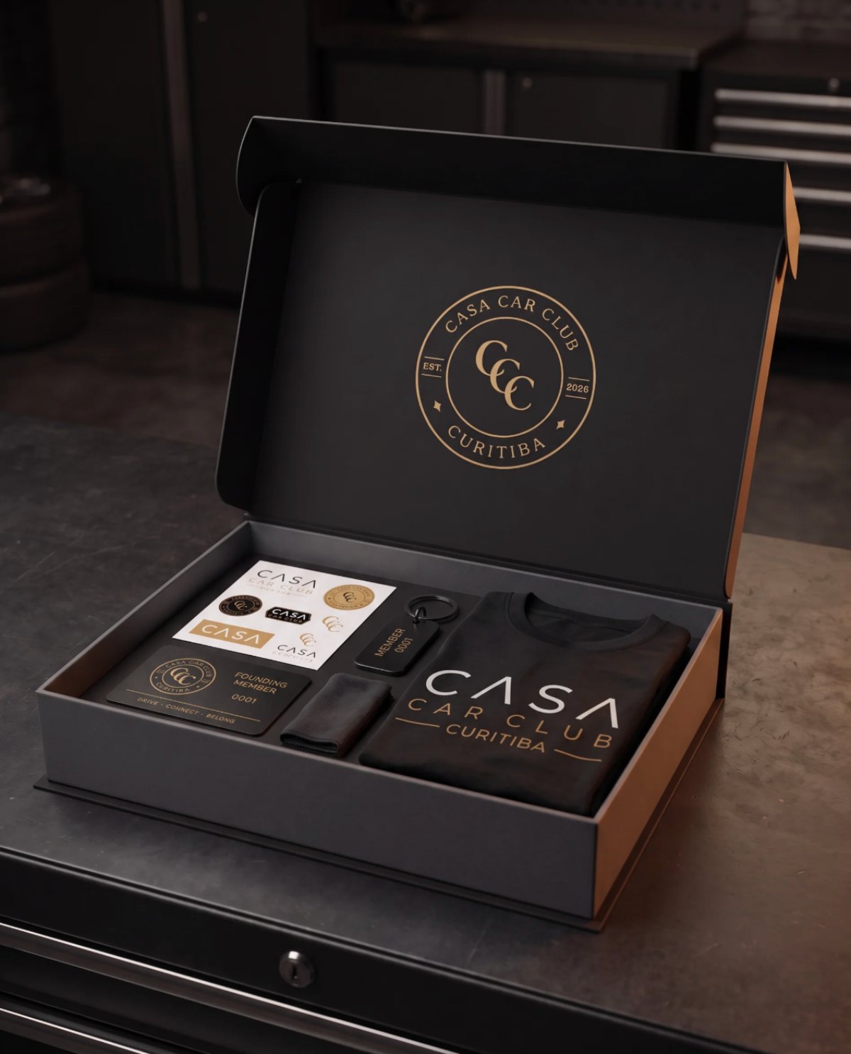 CASA Box Ouro aberta, com camiseta, cartão de founding member, adesivos e chaveiro.